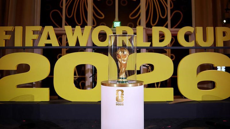 The World Cup trophy on display on a white stand prior to the draw in December in Washington with Fifa World Cup 2026 in big gold letters in the background.