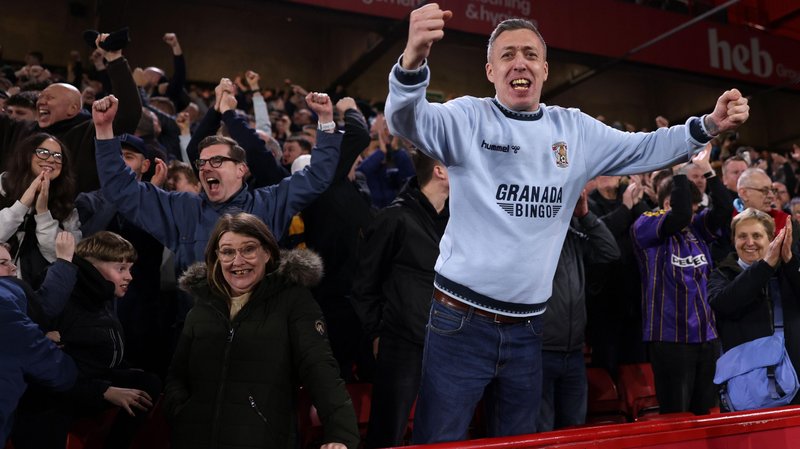 Coventry City fans celebrate a goal during the 2-1 win at Sheffield United on 25 February with one supporter, wearing a sky blue Coventry sweatshirt, standing on his chair, spreading his arms out with pumped fists and a big smile on his face