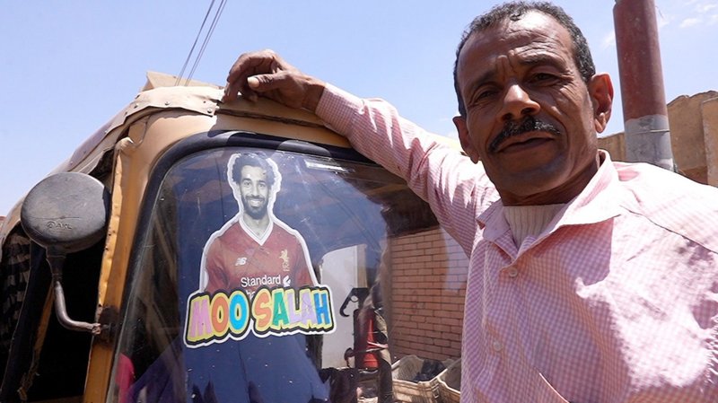 A tuk-tuk driver in Nagrig, Egypt, poses in front of his vehicle which has a sticker of Liverpool and Egypt winger Mohamed Salah on the windscreen