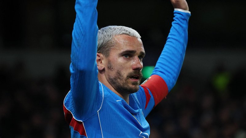 Atletico Madrid forward Antoine Griezmann, with bleached blond hair and facial hair, has both arms raised as he wears blue and red kit
