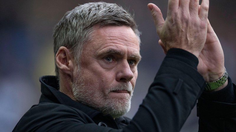 A close up of Graham Alexander applauding wearing a long-sleeved black jacket