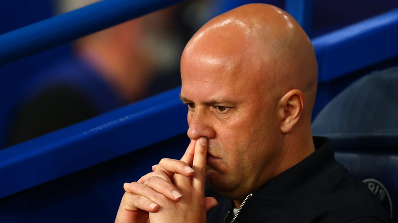 Headshot of Arne Slot, sitting on the bench, fingers on top lip, looking pensive