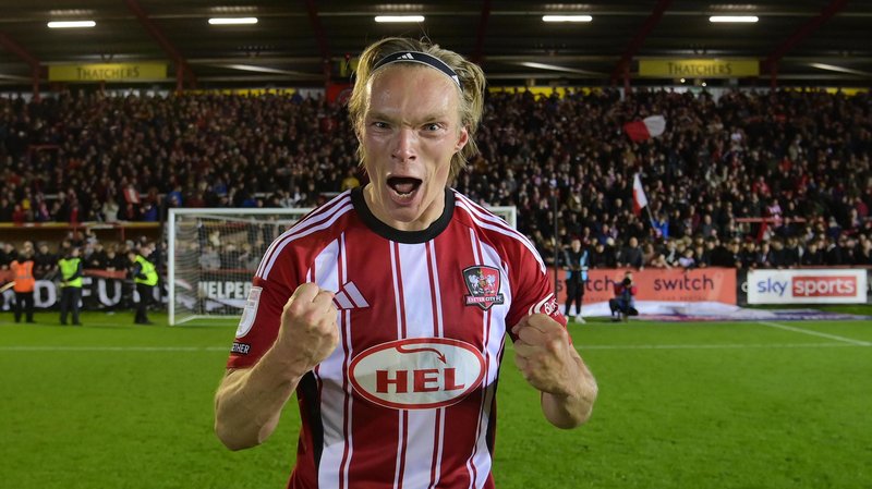 Ilmari Niskanen with clenched fists celebrating in the foreground towards the camera in front of the Exeter fans and the goal nets behind him.