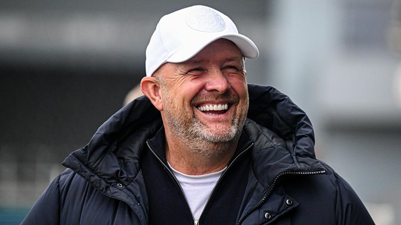 Bromley boss Andy Woodman, wearing a dark coat and a white baseball cap, grins