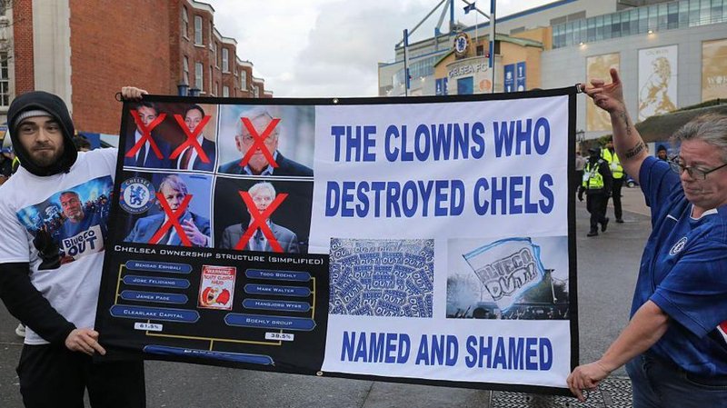 Two Chelsea fans hold up a banner critical of the club's owners, reading 