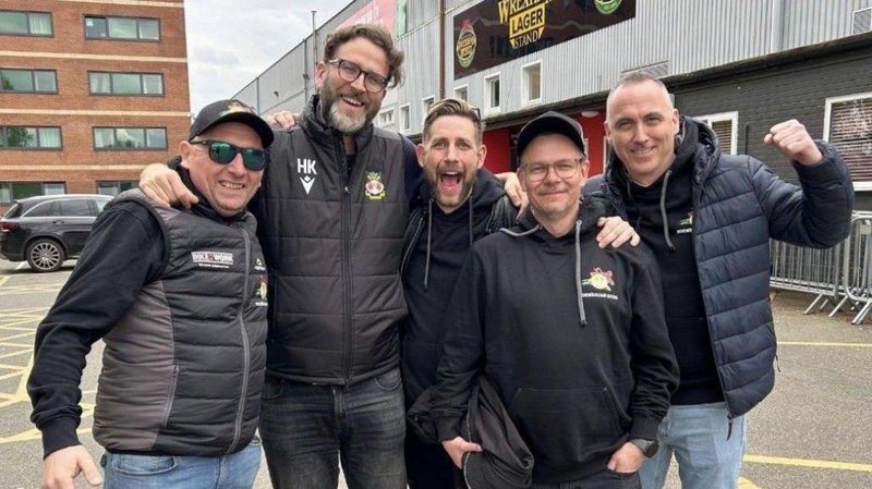 Norwegian fans smile and celebrate outside the Racecourse football ground with Wrexham AFC director Humphrey Ker