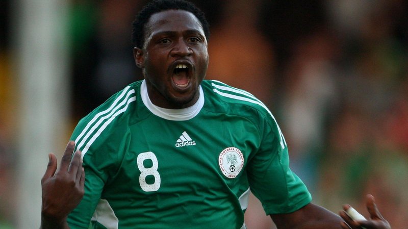 Michael Eneramo shown from waist up, wearing a green Nigeria shirt with white trim, the number eight on the right of his chest and Nigeria crest on the left, holds his hands up and is seen with his mouth open in celebration after scoring a goal