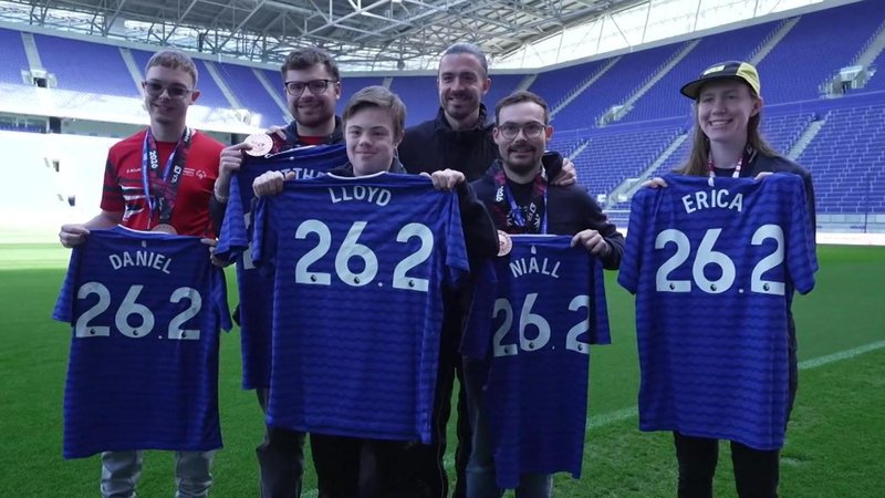 Jack Grealish poses for a photo with five athletes from Special Olympics Great Britain. They are all holding up Everton shirts with '26.2' on. 