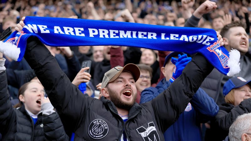 An Ipswich fan holds up a blue scarf with white writing which reads 
