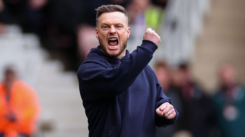 Kim Hellberg, wearing a navy blue sweatshirt, has his mouth open shouting while punching his right hand in the air and clenching his left fist to celebrate a Middlesbrough goal