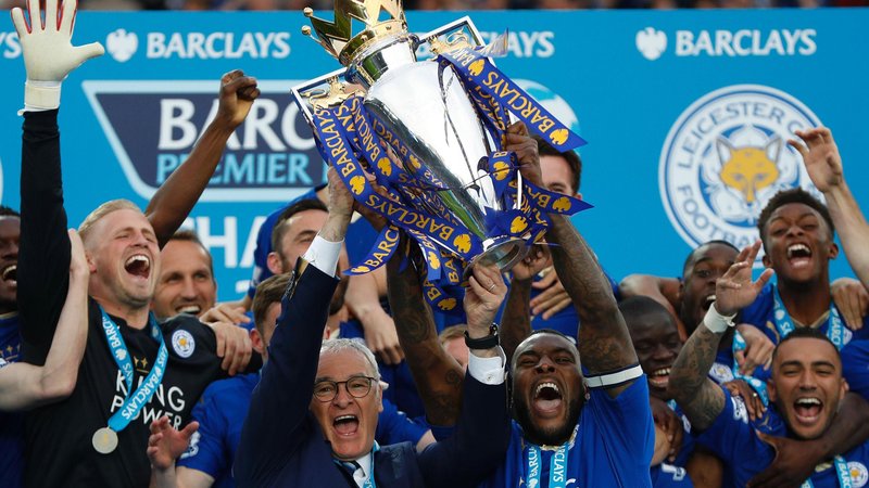 Leicester City manager Claudio Ranieri and captain Wes Morgan lift the Premier League trophy while surrounded by euphoric Foxes players