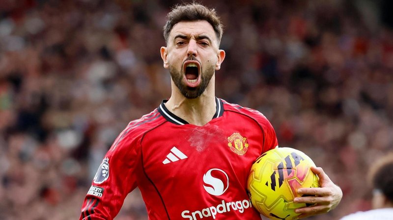 Bruno Fernandes celebrates a goal for Manchester United, with his mouth wide open and the ball in his left hand