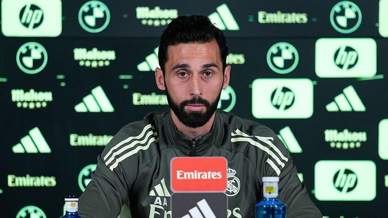 Alvaro Arbeloa speaks at a Real Madrid news conference, in dark green training outfit with light green trim, in front of an advertising board in same colours