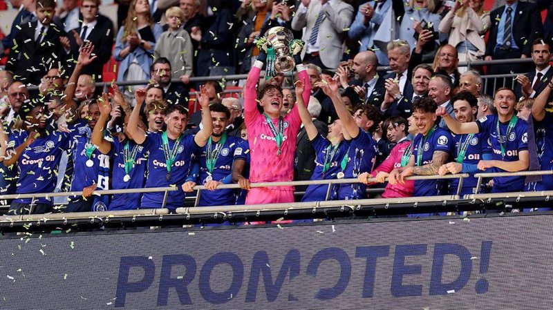 Oli Whatmuff lifts the National League promotion final trophy above a sign saying 'promoted'