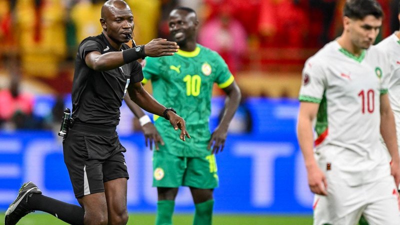 Referee Jean-Jaques Ndala, dressed in all-black kit and with a whistle held between his lips, points with his right hand for a penalty as he runs behind Morocco's Brahim Diaz, who dressed in white kit with red and green trim, after awarding a controversial spot-kick to Morocco in the final of the 2025 Afcon.