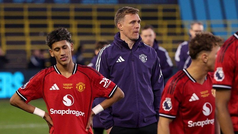 Manchester United Under-18 coach Darren Fletcher, in purple tracksuit top, stands between two of his players, who both wear red match kit
