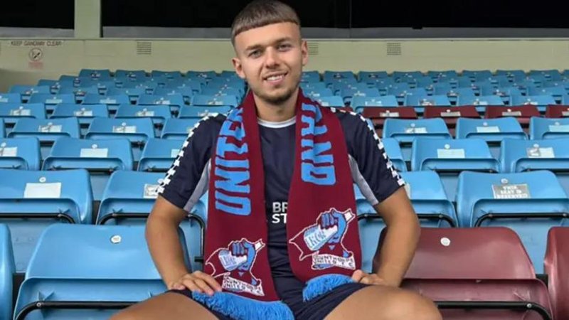 Jonathan Gjoshe sitting in the stands at Glanford park wearing blue shorts and shirt and a Scunthorpe United scarf