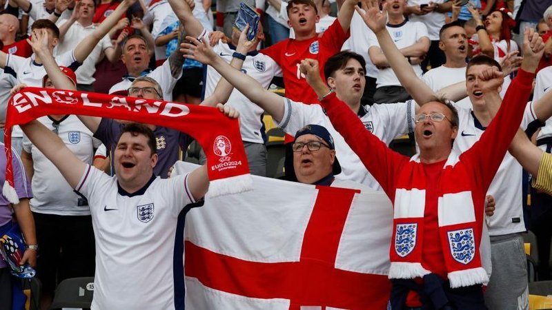England fans before the Euro 2024 final, many wearing white team shirts, while some have scarves and one holds a red and white Cross of St George flag