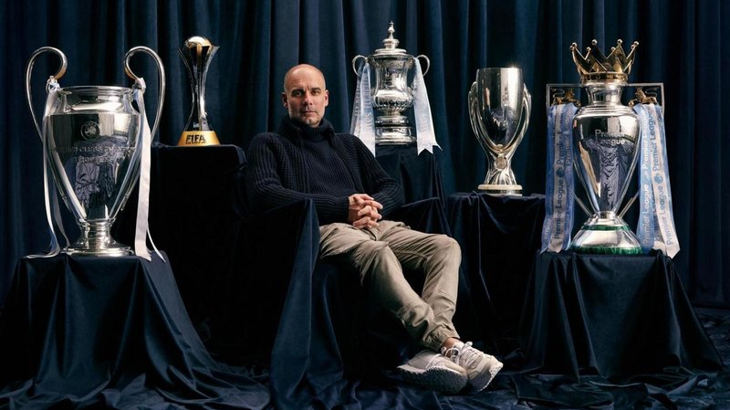 Pep Guardiola sitting down with trophies around him