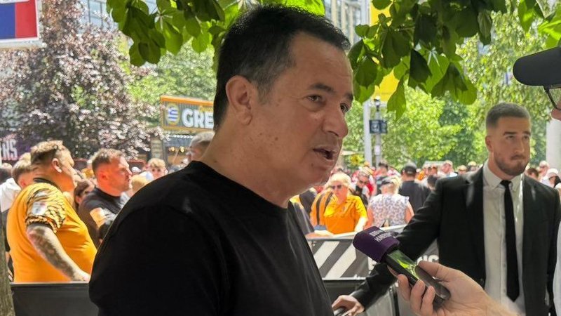 Hull City owner Acun Ilicali being interviewed outside Wembley Stadium, wearing a black t-shirt. Crowds on Olympic Way can be seen behind him.